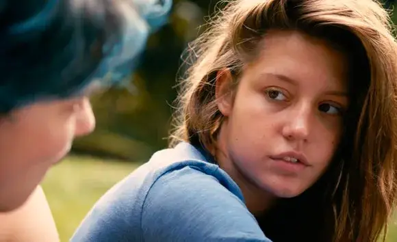 A scene from Blue Is the Warmest Color, where a young woman gazes at her lover with intense desire in a park. Her lover, with striking blue hair, appears in a soft blur, adding an ethereal quality to their connection.