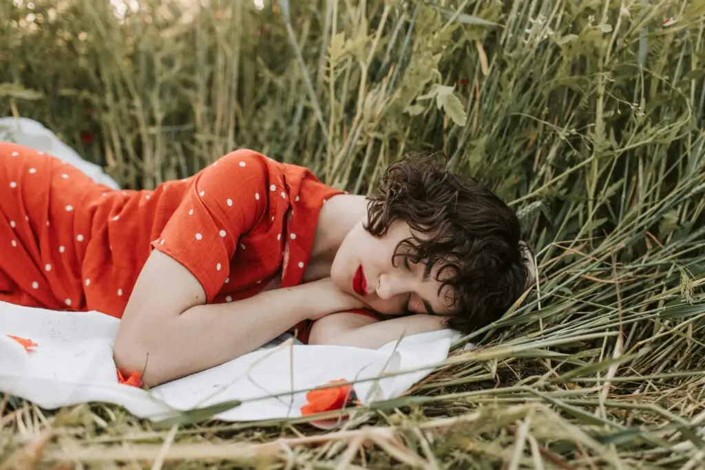 An elegant woman with a red dress and lip stick sleeps on the grass while learning French with FeelGoodFrench