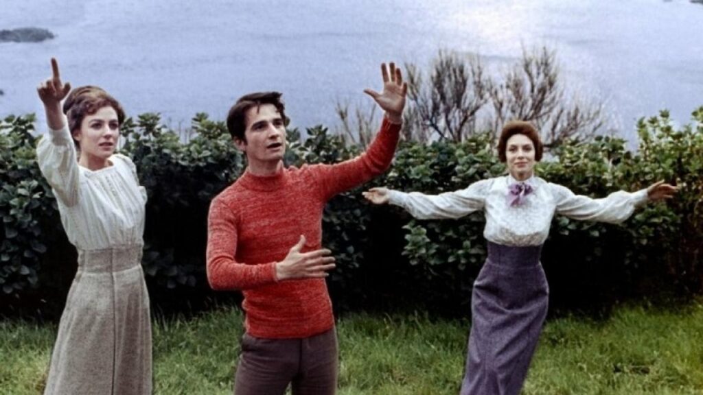 Three protagonists in fancy clothing from the movie Les Deux Anglaises et le Continent dancing in a lush coastal countryside, embodying joie de vivre, love, and the complexities of their intertwined relationships.