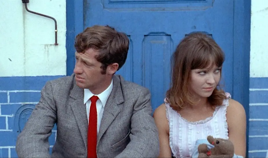 Scene from the French New Wave film Pierrot le Fou showing two lovers looking in opposite directions, on the verge of exchanging romantic words in French.