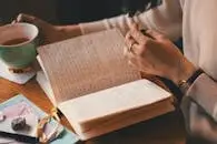 pexels-photo-3363111-3363111 A woman writes in a journal while enjoying a cup of coffee at a wooden table.