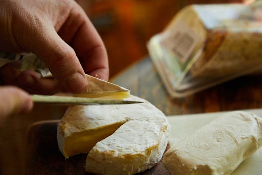 A close-up of hands slicing creamy French Brie cheese on a wooden board. 