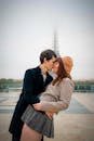 Couple sharing a romantic kiss before the iconic Eiffel Tower on a cloudy day in Paris.