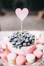 A pink blueberry cake topped with fresh berries and surrounded by macarons, perfect for a romantic setting.