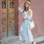 A fashionable American expat woman stands with baguettes in France, wearing a floral dress and hat in a city environment in the French riviera in Nice.