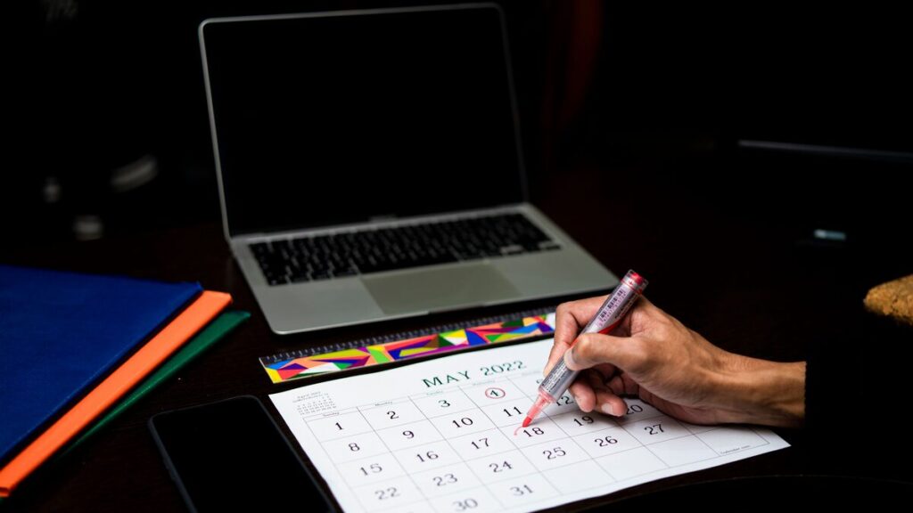 Person marking an appointment date on a calendar beside a phone