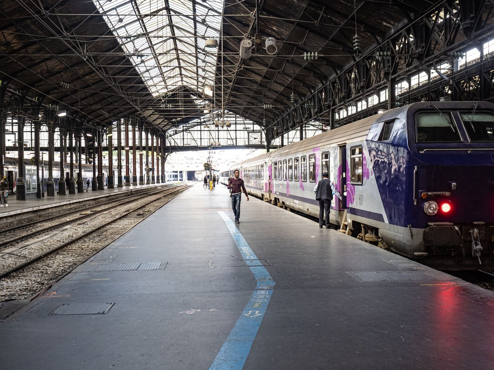 Train and passengers beside a platform under the roof of a Paris railway station