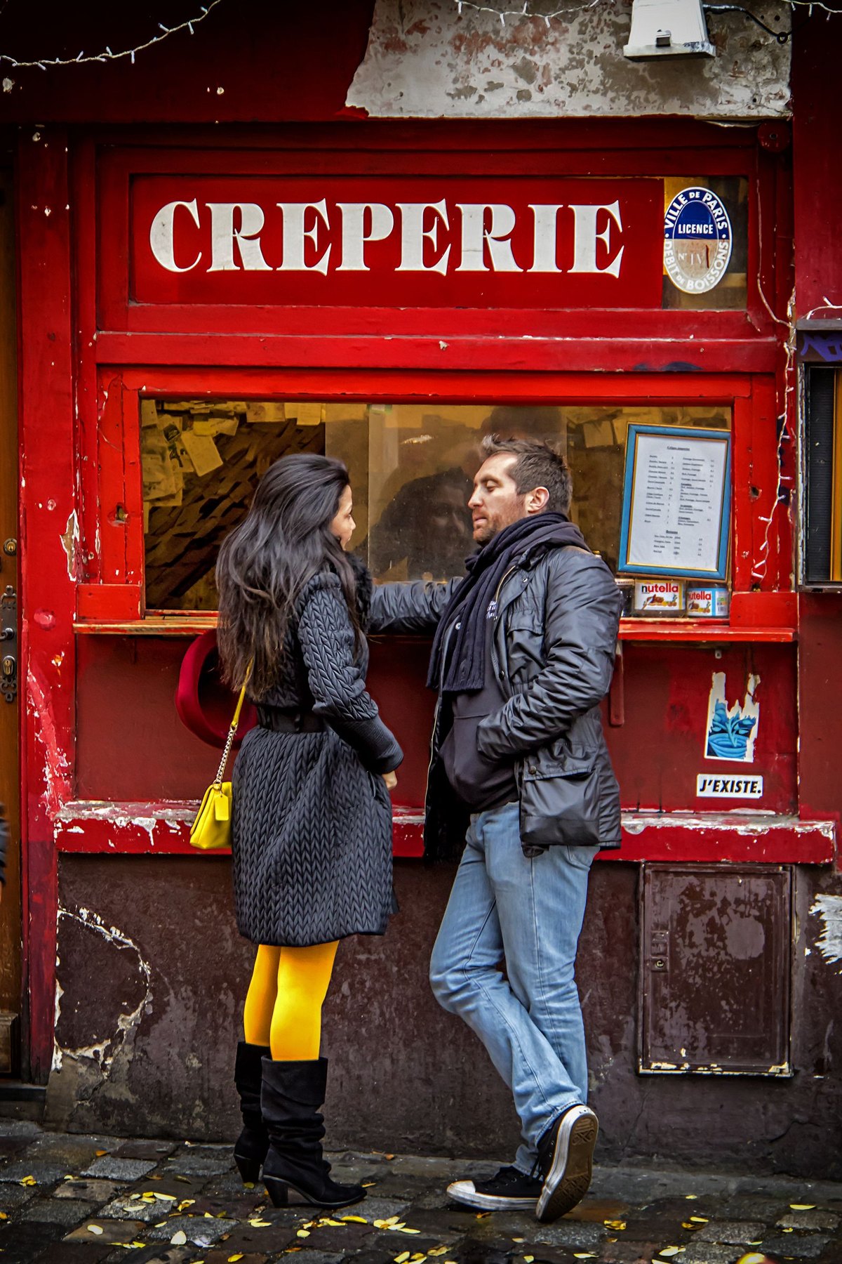 Two people talking outside a red-fronted crêperie in Paris