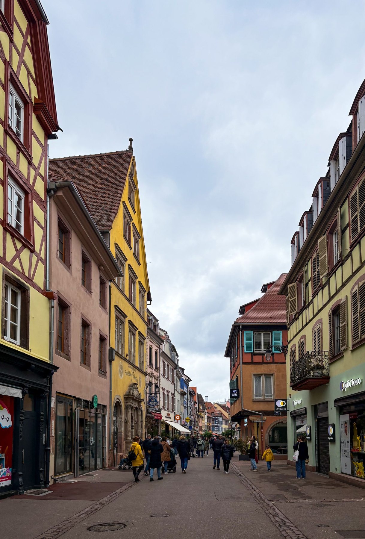People walking along a French town street lined with colourful historic buildings