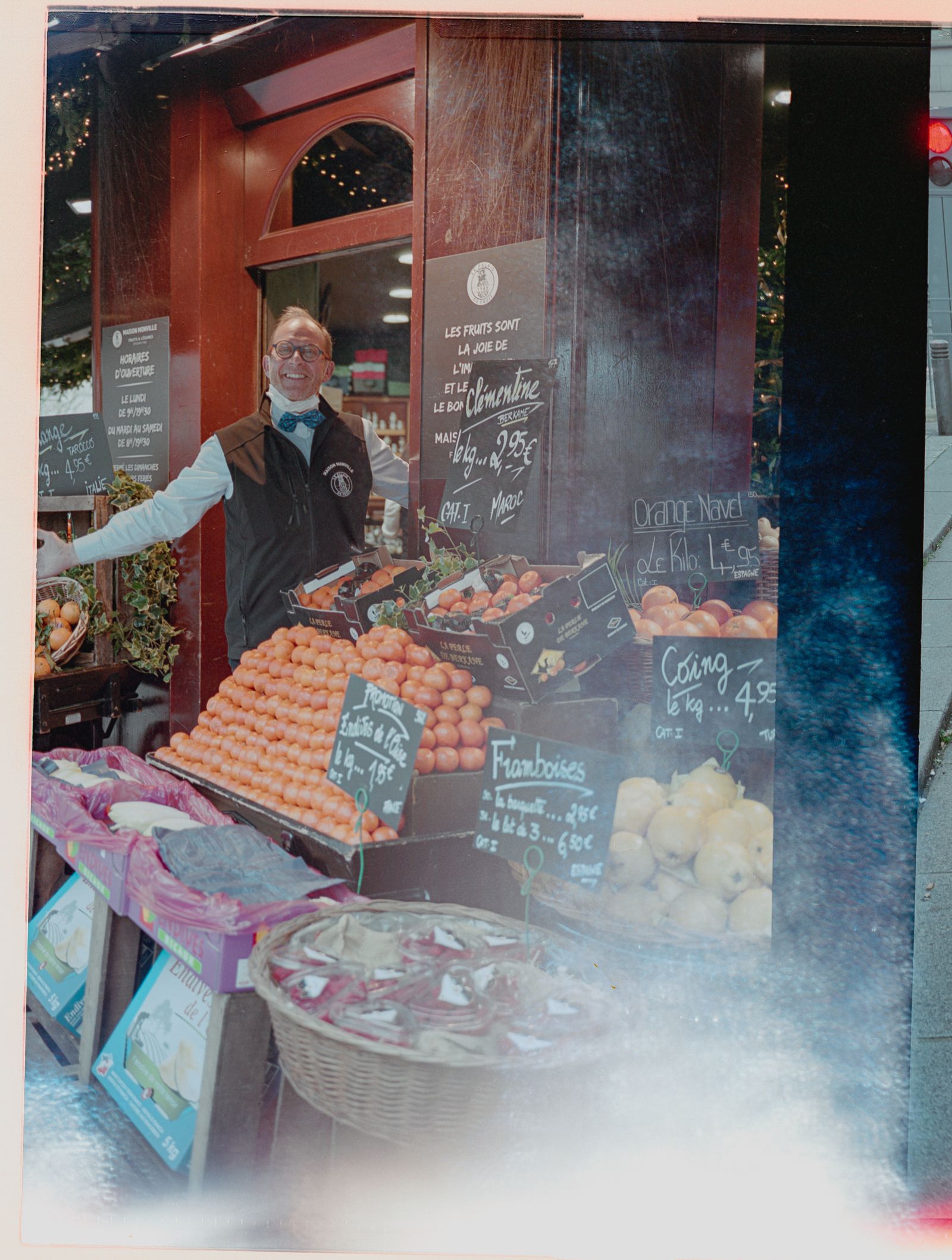 Fruit merchant beside a display of oranges and handwritten signs at a Paris market